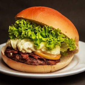 Close-up of a gourmet cheeseburger with fresh lettuce, mayonnaise, and beef patty on a white plate.